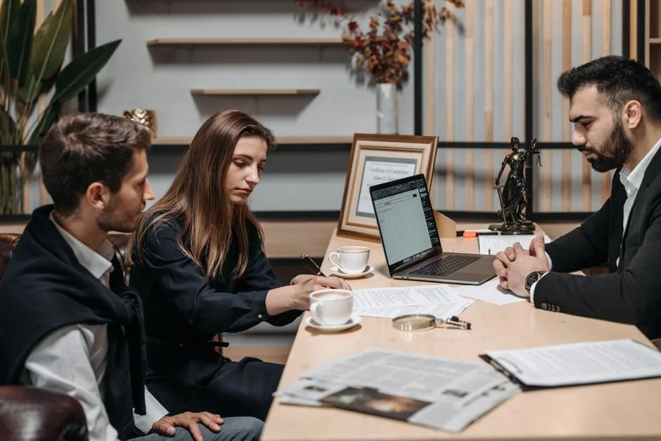 Drei Personen besprechen Unterlagen und einen Laptop bei einem Termin